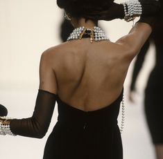 the back of a woman's dress with pearls on her neck and hands behind her head