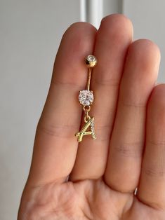 a person holding a gold and white diamond initial charm with the letter a on it