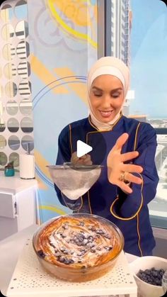 a woman is making a pie in front of a window with the city skyline behind her