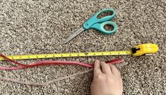 someone is measuring the length of a pair of scissors on carpeted floor with tape