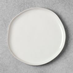 an empty white plate sitting on top of a gray tableclothed surface with no one around it