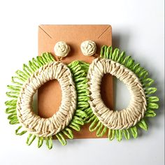 a pair of green and white earrings on top of a piece of brown paper next to a card