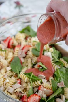 someone is pouring dressing into a salad with strawberries and spinach leaves in it