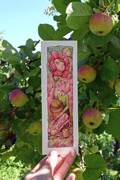 a person holding up a card in front of some fruit trees