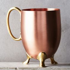 a copper colored coffee mug with a gold handle on a concrete surface, ready to be used as a drink holder