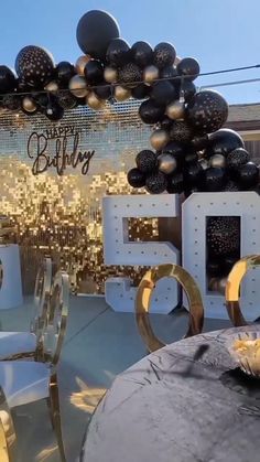 an outdoor birthday party with black and gold balloons, silver chairs and large letters that spell out happy 50th