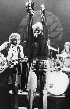 two men on stage with guitars and one man holding up his hands in the air