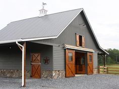 a large gray barn with two doors and a porch on the side of it, in front of a green field