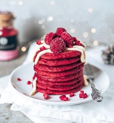 a stack of red velvet pancakes with raspberries on top and white icing