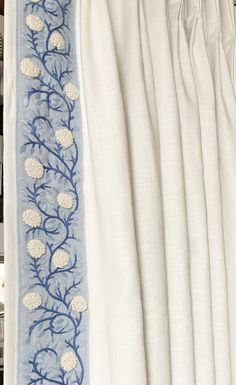 the curtains are lined up with blue and white embroidered designs on them, along with bookshelves in the background