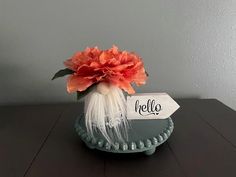 a vase filled with flowers on top of a wooden table next to a sign that says hello