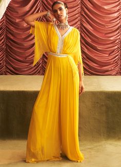 This vibrant Yellow Georgette Embroidered Jumpsuit is perfect for a fun and lively occasion. The draped jumpsuit features intricate embroidery along the neckline and waistline, adding a touch of elegance to the playful silhouette. The wide-leg design and flowy fabric make it ideal for bridesmaids or any bridal event such as a Haldi or Mehendi ceremony. This Indo-Western look is perfect for those looking to stand out while celebrating in style. Composition : Georgette & Lining - Satin Care: Dry Clean Only and Vacuum Storage This product can be customized for sleeves, blouse length and neckline Delivery : 4-6 weeks as the product is hand crafted. Check Size Guide or choose MySize for free customisation (All Sizes above XL can be made at 15% additional cost) For more information and sizes ple Draped Jumpsuit, Mehendi Ceremony, Sangeet Outfit, Embroidered Jumpsuit, Vacuum Storage, Ready To Wear Saree, Indian Wedding Wear, Flowy Fabric, Western Look