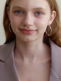 a close up of a person with blue eyes wearing a suit and large hoop earrings