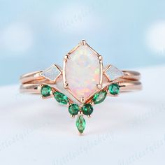 an opal and emerald ring on a white surface