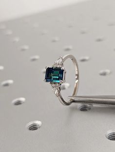 a ring with an emerald colored stone in the center and diamonds around it on a silver surface