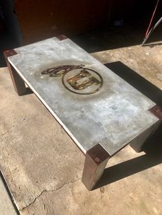 a metal table sitting on top of a cement floor next to a building with an emblem painted on it