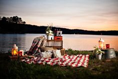 a picnic on the shore of a lake at sunset with blankets, candles and flowers