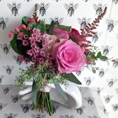 a vase filled with pink flowers sitting on top of a white table covered in bees