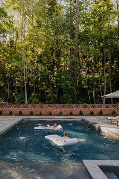 two people floating on inflatable rafts in a swimming pool surrounded by trees