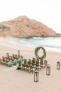 an outdoor ceremony setup on the beach with chairs and wreaths in front of it