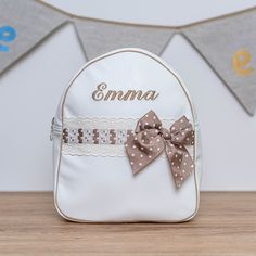 a white backpack with a brown bow and name on the front, sitting on a wooden table