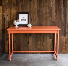 an orange table with a black frame on top and a white vase next to it