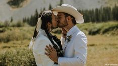 a man in a white suit and cowboy hat kissing a woman with braids on her head