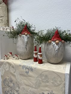 two pots with plants in them sitting on a table cloth next to some gnome figurines