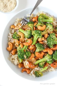 a white bowl filled with broccoli and cashews next to a spoon