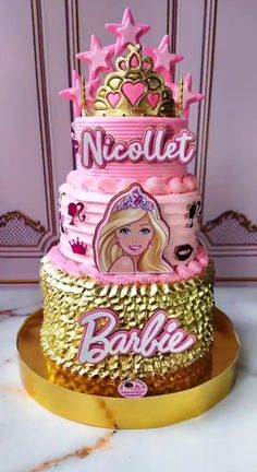 a three tiered cake decorated with barbie dolls and gold trimmings on a marble table