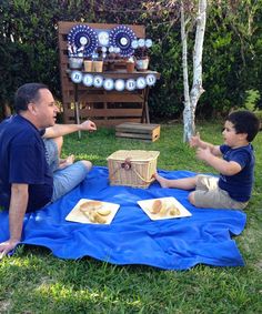 two men sitting on a blanket in the grass eating food and talking to each other