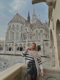 a woman standing on top of a stone wall next to a building with a clock tower