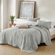 a bed with white sheets and pillows in a room next to a plant on the floor