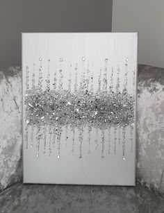 a white canvas with silver sequins on it sitting on a gray velvet couch