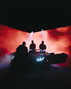 three people sitting on top of a car in front of a red wall with fog