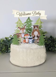 a welcome baby cake with woodland animals on top and pine trees in the back ground