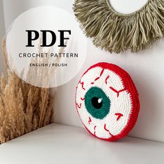 a crochet eyeball is sitting next to some dried grass and a round mirror