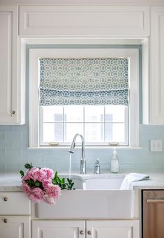 a white sink sitting under a window next to a counter top with flowers in it