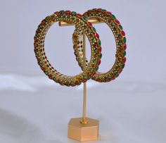 These are premium quality handcrafted bangles embellished with beautiful ruby and emerald stones that exude classic sparkle. They are the perfect accompaniment to a Kundan kada, elevating your saree or ethnic outfit to a stunning level. Openable Kada. You can go one size up or down. Size: 2.6 (Diameter: 6.1 cms) & 2.8 (Diameter 6.4 cms) Screw Opening Width: Approx. 1/2" Comes as a Pair or Single. 1 GM Gold plated on high-quality brass as the base metal. *Color may vary slightly due to light cond Jadau Kada, Kundan Kada, American Diamond Ring, Contemporary Bracelets, Photography Jewelry, American Diamond Necklaces, Bangles Gold, Contemporary Necklace, Contemporary Earrings