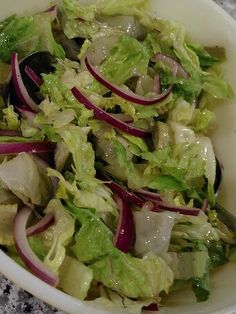 a salad with lettuce and onions in a bowl on the counter top, ready to be eaten