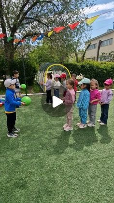 children are standing in the grass with balls and streamers around them, while an adult is