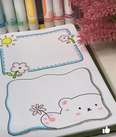 a drawing book with markers and crayons in the background