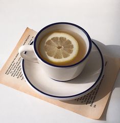 a cup of tea with a slice of lemon in it sitting on top of an open book