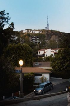 the hollywood sign is on top of a hill behind a car and people walking down the street