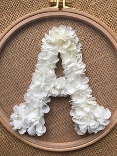 the letter a is made up of white flowers in a wooden hoop on a burlock