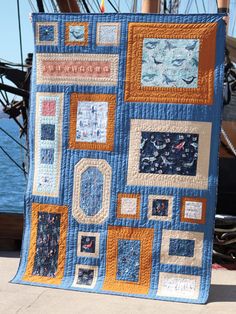 a blue and orange quilt is hanging on the side of a boat in the water