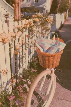 a bicycle parked next to a white picket fence with flowers growing on the side and an umbrella in the basket