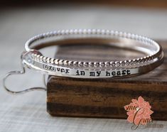 "This beautiful handmade bangle bracelet set is made of sterling silver (92.5%). Includes 3 sturdy bangles, one dot bangle, one rounded hammered bangle and one flat stamped bangle. It is all held together with a hand crafted sterling silver heart (you may add additional hearts in the drop down menu). The flat bangle is stamped with \"forever in my heart\" along the outside, and the name of your loved one is stamped along one side of the heart. These bangles are handcrafted in the size you reques Sterling Silver Stackable Bangle For Anniversary, Stackable Sterling Silver Bracelet For Anniversary, Sterling Silver Bracelet For Mother's Day Anniversary, Nickel-free Sterling Silver Bangle For Wedding, Hand Stamped Sterling Silver Bracelets For Mother's Day, Adjustable Sterling Silver Bracelet For Anniversary, Hand Stamped Bangle Jewelry, Mother's Day Hand Stamped Sterling Silver Bracelets, Silver Stackable Bracelets For Mother's Day