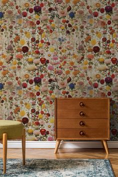 a floral wallpaper with an old dresser in the foreground and a green chair on the far side