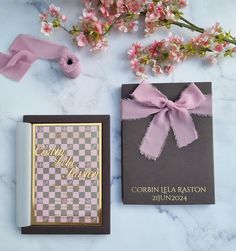 two books with pink bows on them sitting next to some flowers and a bow tie